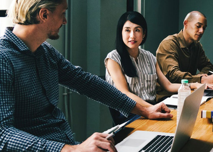 three people sitting at a table with their laptops talking to each other